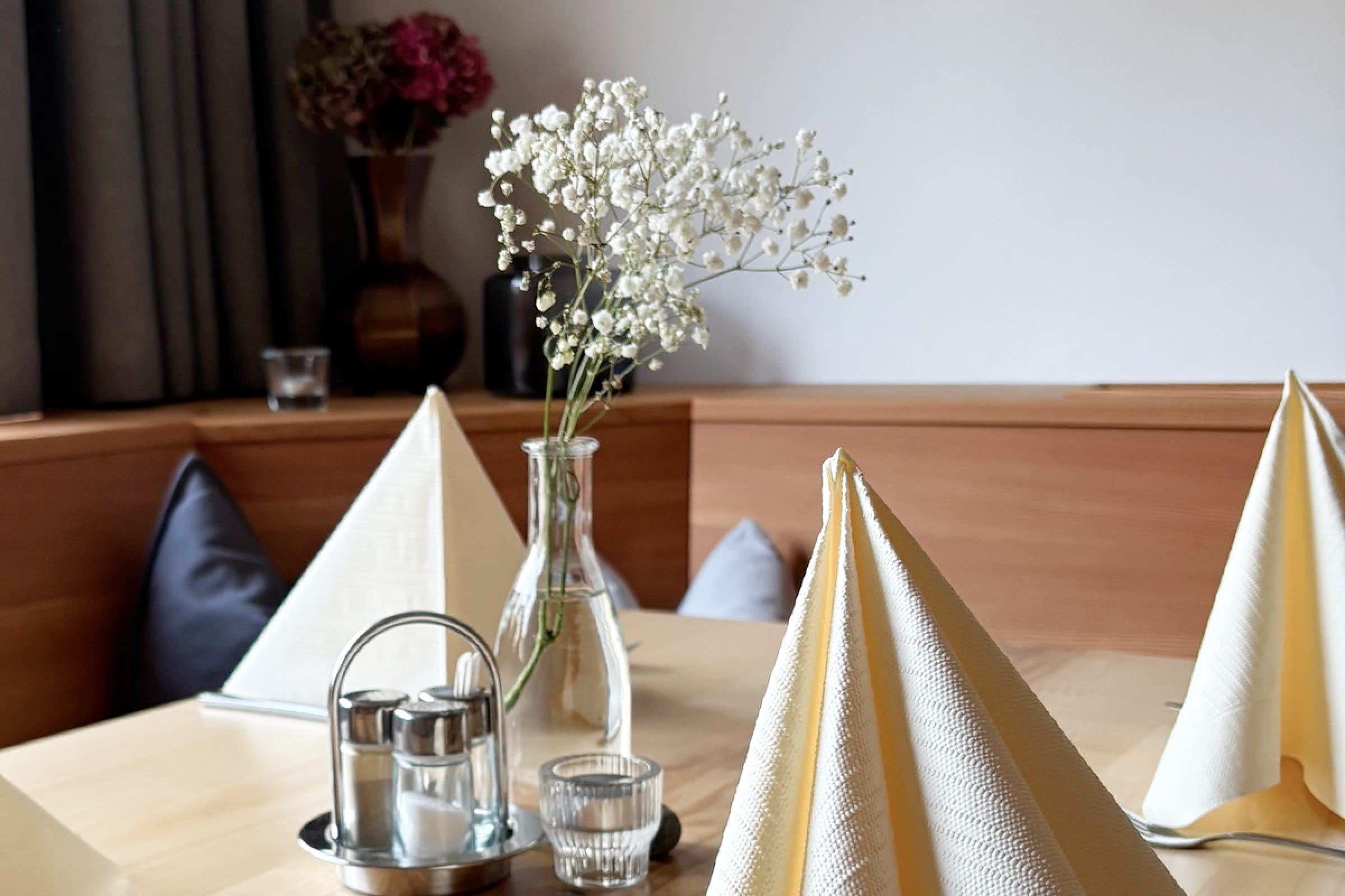 Tisch mit gefalteten Servietten, Glasvase mit Schleierkraut und Salz- und Pfefferstreuer in unserem Gasthof.