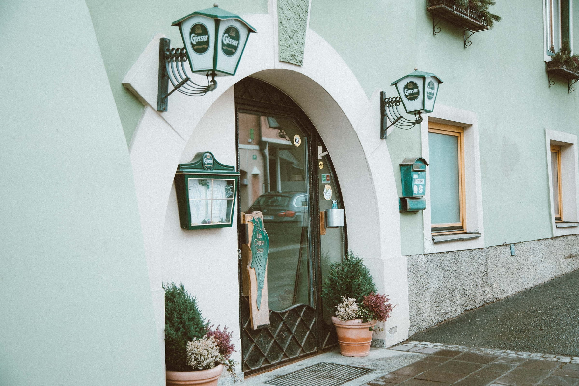 Eingang unseres Gasthofs mit bogenförmiger Tür, zwei Laternen und Pflanzen in Töpfen davor.