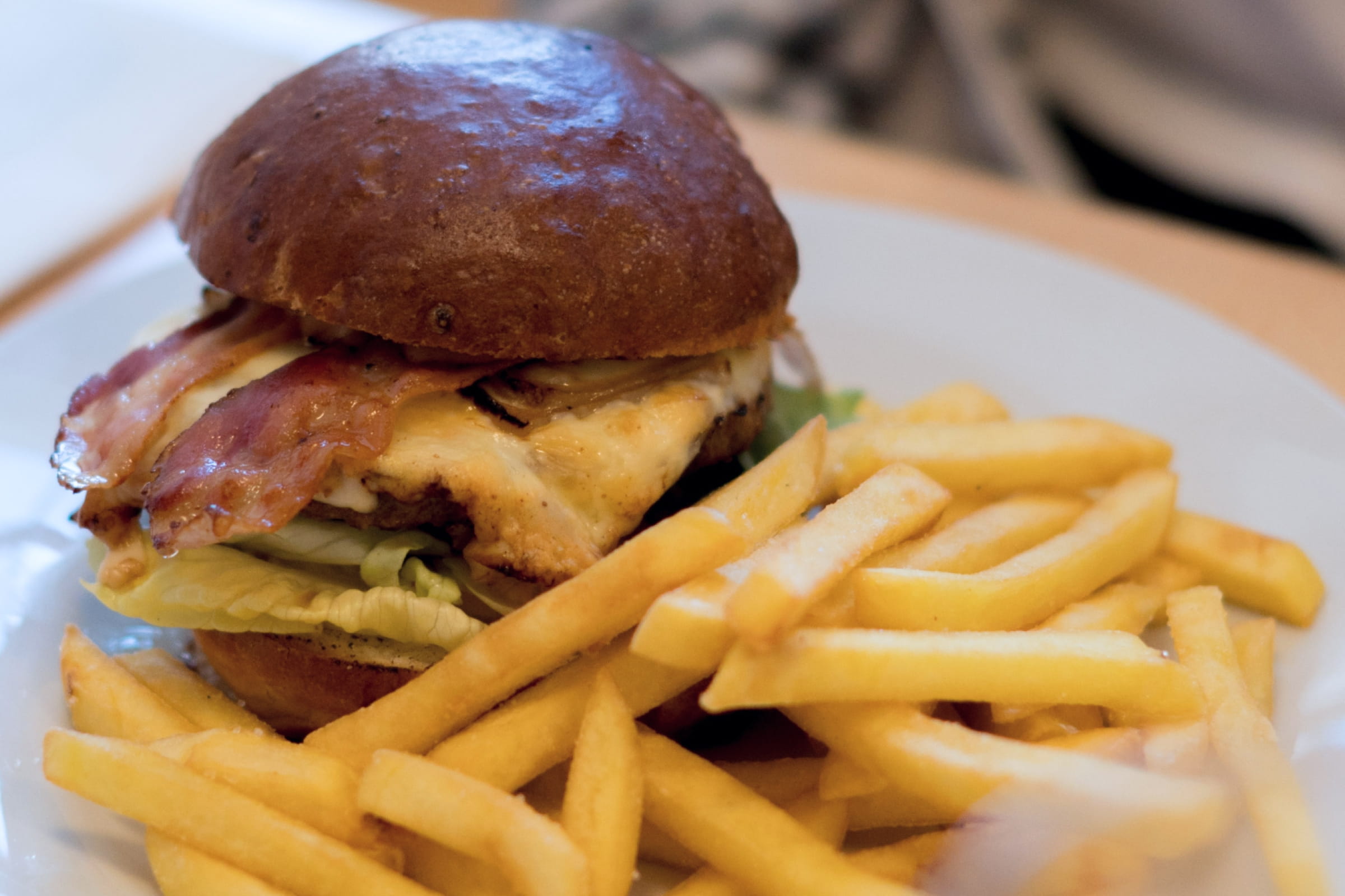 Burger mit Salat und Speck auf einem Brötchen neben Pommes frites auf einem weißen Teller