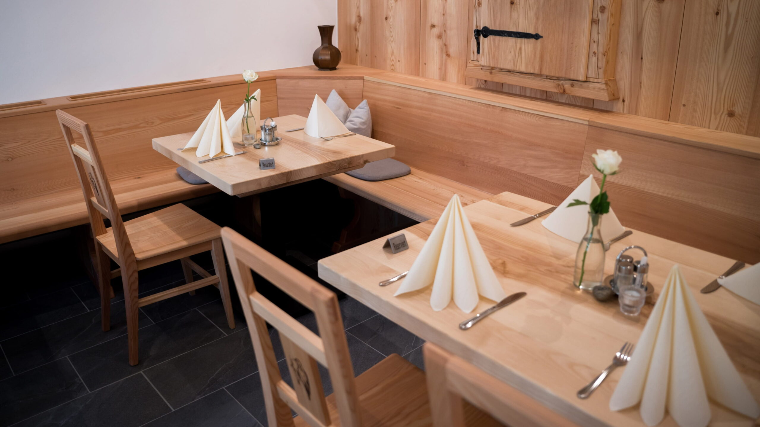 Gedeckte Holztische mit gefalteten weißen Servietten, Holzstühlen und einer Holzbank in unserem Restaurantinnenraum.